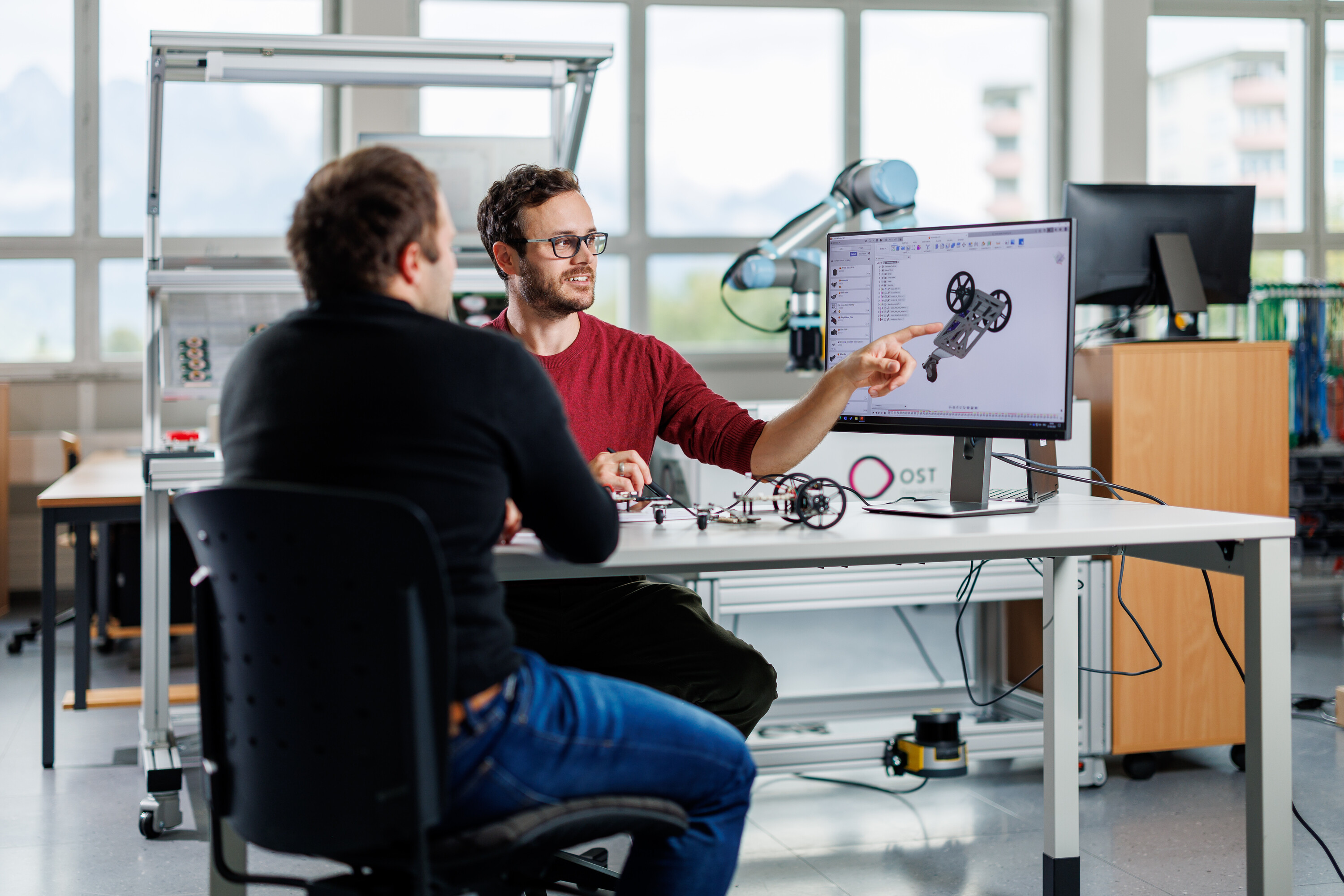Zwei Männer diskutieren vor einem Monitor mit einer CAD-Zeichnung (Symbolbild für MSE Ingenieurstudium)