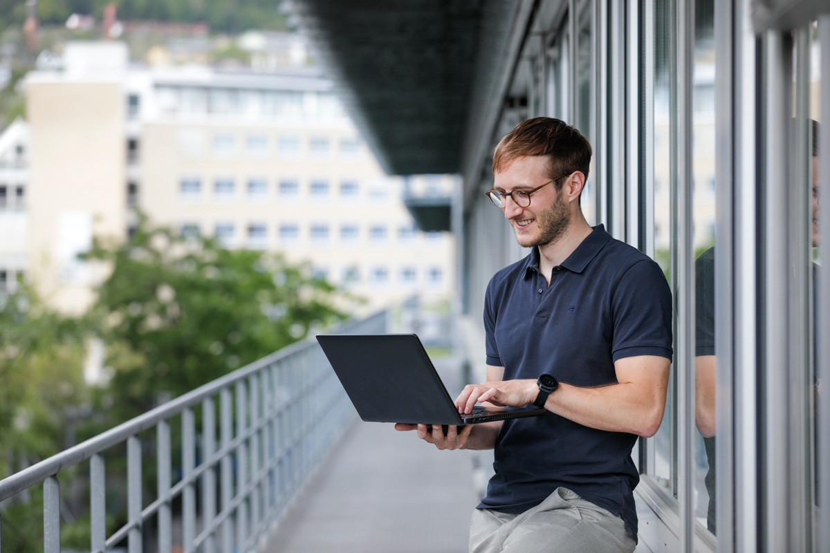 Junger Mann mit Laptop, auf Balkon stehend